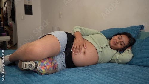 Pregnant woman with prosthetic leg relaxing on bed