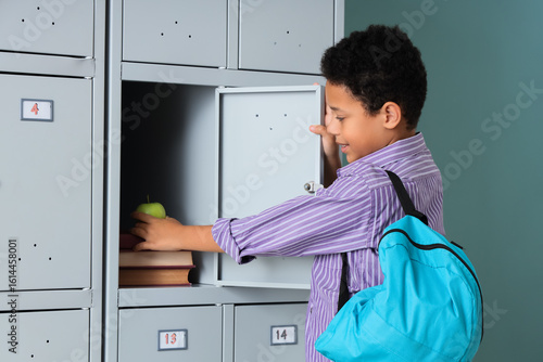 Teenage African-American schoolboy taking apple from locker on mint background