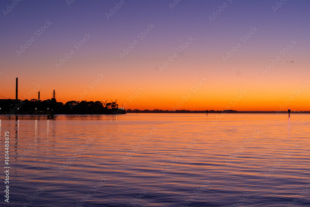 Naklejka premium Ferry dock in Geelong for the Spirit of Tasmania with industrial cranes in the background as the sun sets over the Bass Strait in Victoria, Australia