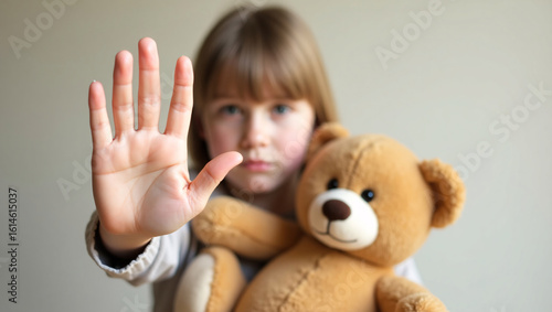A child raising their hand to protect themselves, holding a teddy bear, a poignant message of safeguarding