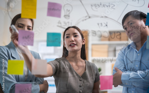 Asian business team in a creative meeting, collaborating and sharing ideas using colorful notes on a glass wall. A modern teamwork setting showing brainstorming, innovation, and planning in office