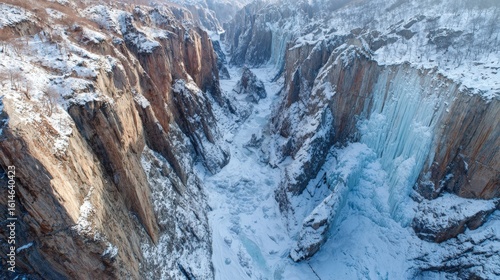 A breathtaking view of a vast canyon filled with ice and snow on a clear winter day. The cliffs tower over the frozen river, showcasing nature's winter beauty in a remote area