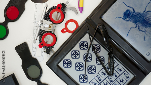 Arrangement of optometry measurement tools for eye examination. Stereo vision test, retinoscope, ophtalmoscope, volk lens, trial frame and lens, prism bar, projector remote, polarizing filter.