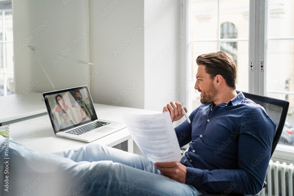 Smiling businessman discussing with colleagues in meeting on video call at office Smiling businessman discussing with colleagues in meeting on video call at office