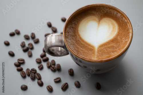 Heart shape Latte art in a ceramic cup  place on gray background  with copy space left, there are coffee beans around