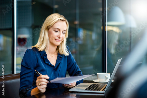 Smiling mature businesswoman doing paperwork at cafe