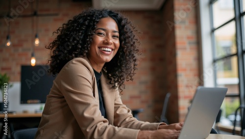 Smiling young Black woman working happily on laptop in modern office space