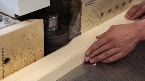 A carpenter guides a piece of pine wood through a spindle moulder, precisely shaping the edge for smoothness and profile, showcasing skilled craftsmanship and control
