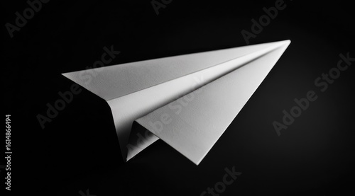 A grayscale close-up shot of a meticulously folded paper airplane, set against a stark black background, emphasizing its form and texture