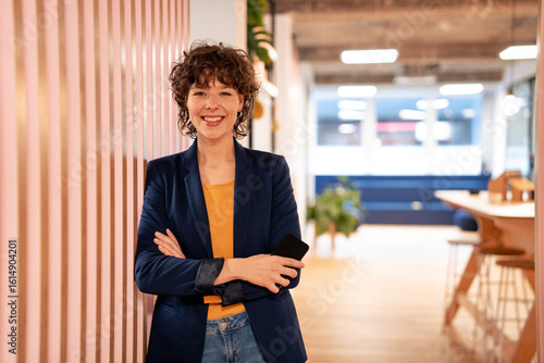 Happy young businesswoman standing with arms crossed near striped wall in office