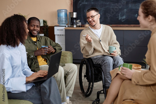Smiling business people siting with coffee cups and having discussion in office
