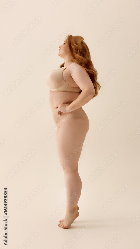 Obraz premium Confident plus-size woman standing in profile on neutral background. Concept of relaxed identity, natural sensuality, inclusive fashion, body empowerment, modern femininity