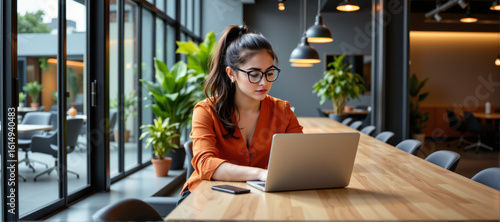 Focused female professional working on laptop modern office digital workspace bright environment side view productivity concept
