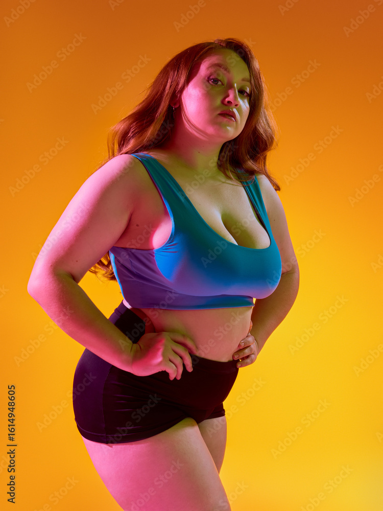 Fototapeta premium Self-assured woman posing against lively orange background. Concept of vivid body expression, radiant energy in fashion campaigns, confident sportswear identity.