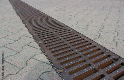A strong storm drain grate on the surface of evenly laid outdoor tiles 

