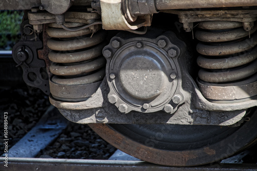 Fotografie Close-up of modern railcar wheelset showcasing robust coil springs, brake assembly, and steel components on track ballast under natural daylight