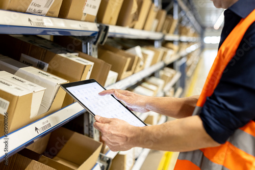 Worker checking inventory through tablet PC by rack in warehouse