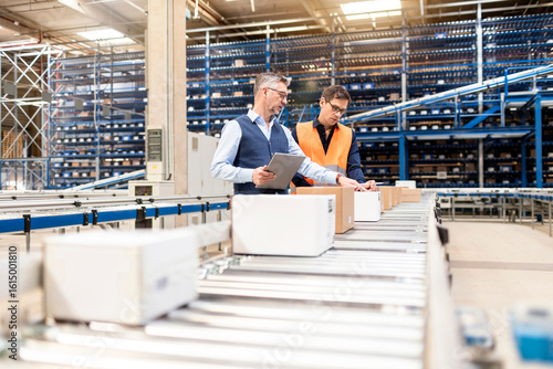 Manager discussing over cardboard boxes with colleague by conveyor belt in warehouse