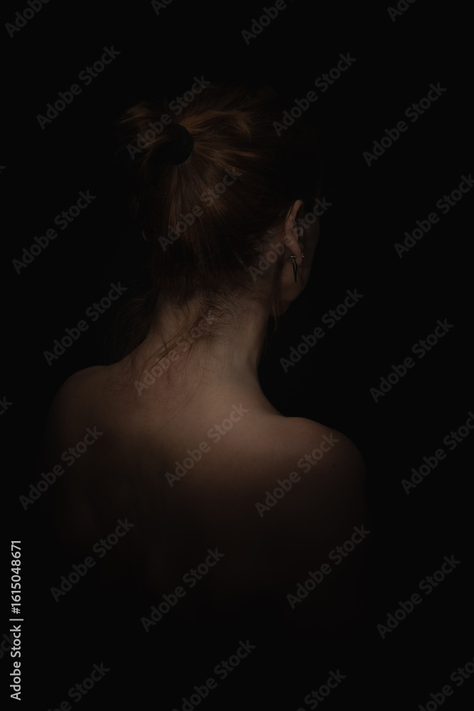 Back view portrait of a woman with tied hair on black background in low lighting Back view portrait of a woman with tied hair on black background in low lighting