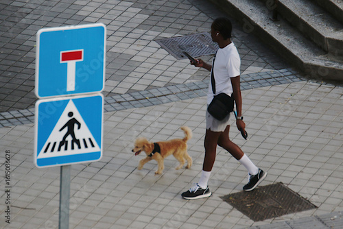 Quadro em tela Hombre negro paseando a su perro por la calle mientras mira su teléfono móvil ju