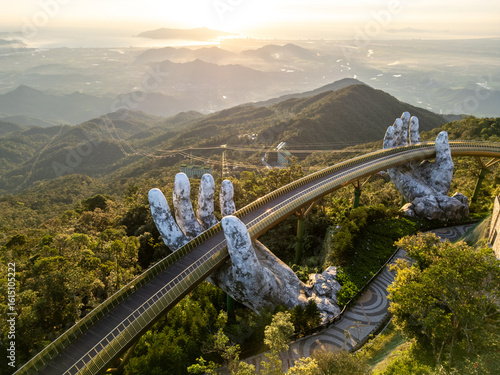 Aerial view of the iconic Golden Bridge, held by giant stone hands, stretching across the lush, sun-kissed mountains, DaNang, Da Nang, Vietnam.