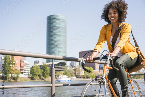 Happy businesswoman riding bicycle by River Main on sunny day