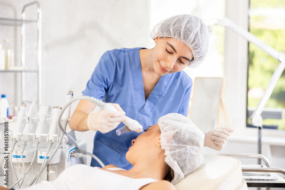Φωτογραφία Positive young female aesthetician applying atomized nutrients with airbrush onto woman client face skin to enhance and revitalize complexion