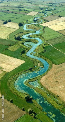 Aerial view of a meandering river snaking through patchwork fields of green and brown, creating a vibrant landscape. Trees cluster along the riverbanks