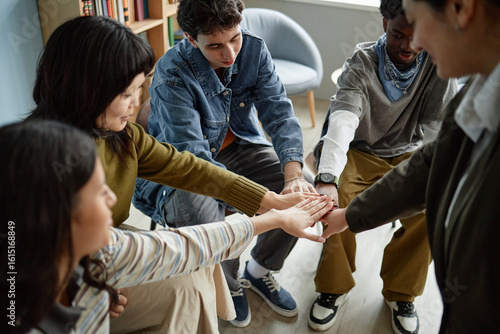 Fotografía Group of diverse teenagers sitting in counseling session joining hands in center