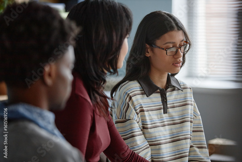 Multiethnic group of teenagers attending counseling session, Black teenage boy and Asian teenage girl sitting together listening to girl wearing glasses