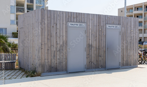 B  timent de toilettes publiques en bois pr  s de la plage avec deux portes distinctes pour hommes et femmes.