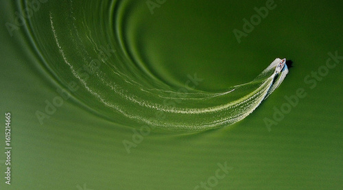 Aerial view of a boat slicing through the murky green water, leaving a swirling white wake in its path, Kharkiv, Kharkiv Oblast, Ukraine.