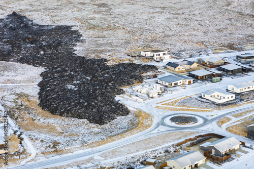 Aerial view of stark black hardened lava flow encroaching on a snow-dusted town, a dramatic contrast of destruction and resilience, Grindavik, GrindavÃ­kurbÃ¦r, Iceland.