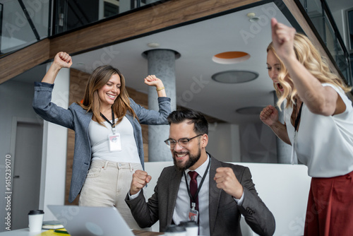 Bild auf Leinwand Excited business team celebrating success with laptop in modern office