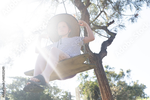 Girl swinging on a handmade swing wearing a big broad brim hat in summer sunshine