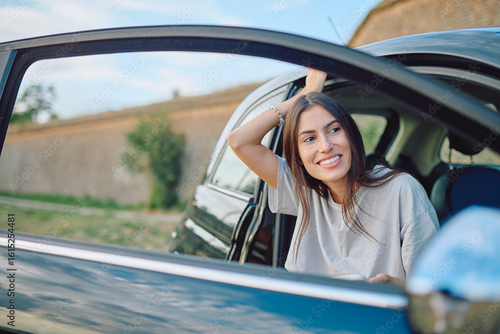 Naklejka premium Carefree female tourist relaxing in a car, gazing out the window and soaking in the beauty of nature during a summer road trip