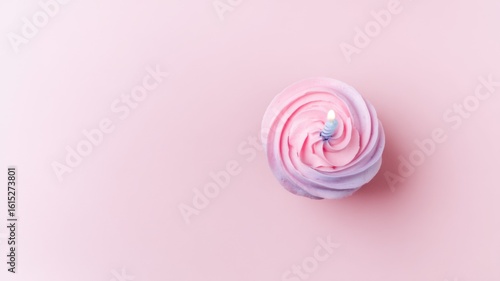 A pastel pink cupcake with floral frosting and a single lit candle, casting a warm glow,