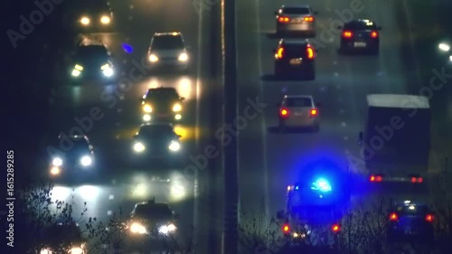 Car lights and parking lights in night traffic on all lanes of the highway going up, where an ambulance with flashing blue lights is going to the hospital