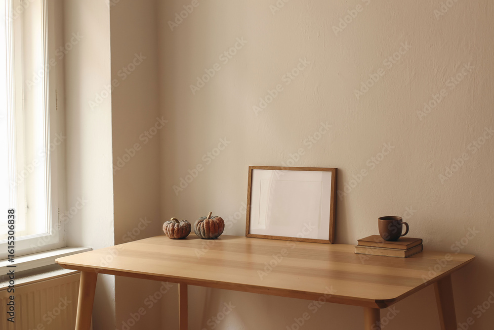 Fototapeta premium Autumn interior still life. Cup of tea, coffee, old books and pumpkins on wooden table at window. Horizontal picture frame, poster mockup. Home office. Minimal Scandi interior. Thanksgiving home decor