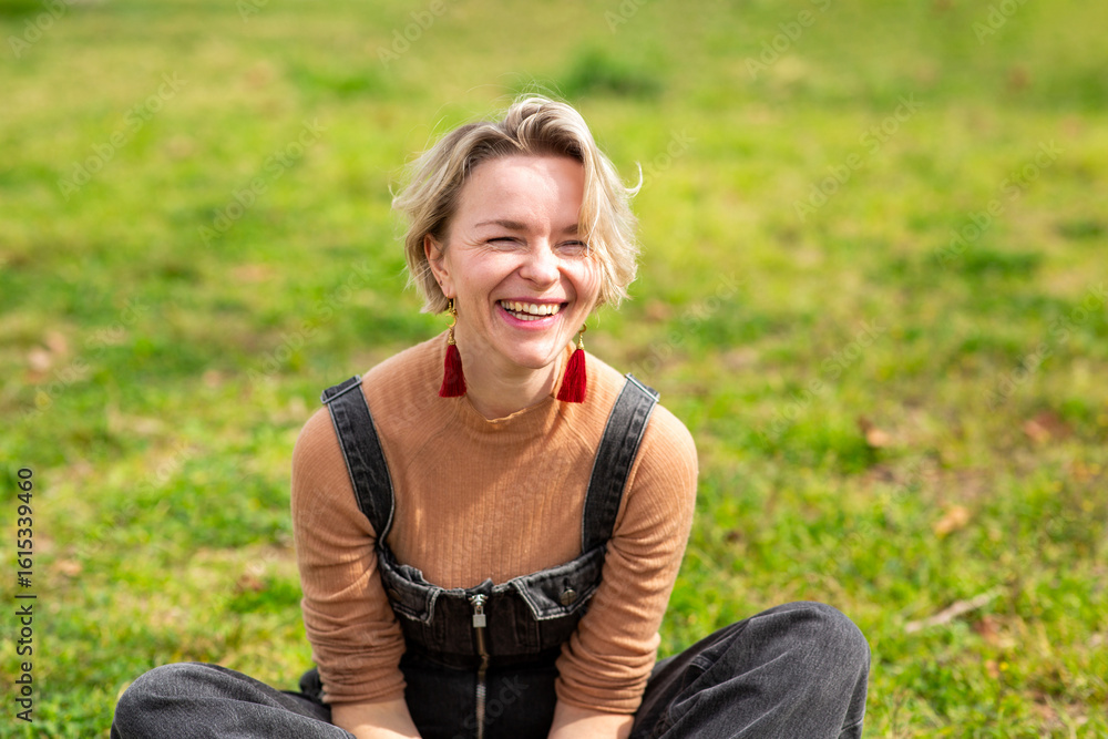 Obraz premium Laughing woman sitting on the grass in sunny park
