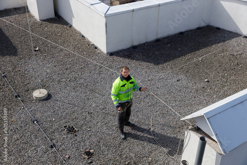 Billede på lærred Worker in Safety Gear on Rooftop: Ensuring Safety Protocols While Using Guiding