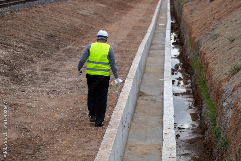 An Asian civil engineer in safety gear supervising a construction project by a railway. An Asian civil engineer in safety gear supervising a construction project by a railway.