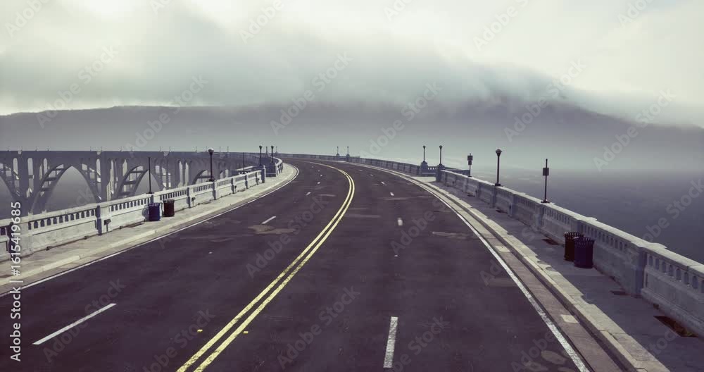 A winding coastal highway stretches towards a bridge, enveloped in fog. The scene captures a tranquil atmosphere with blurred mountains in the background, creating a sense of mystery. A winding coastal highway stretches towards a bridge, enveloped in fog. The scene captures a tranquil atmosphere with blurred mountains in the background, creating a sense of mystery.