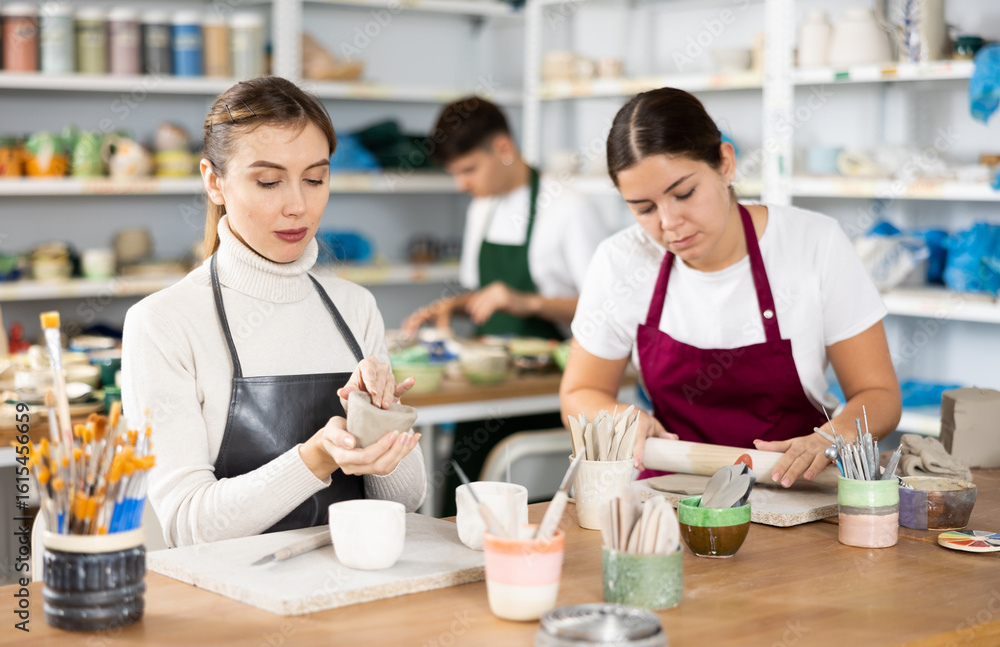 Fototapeta premium Two young women in apron modeling clay pottery in workshop