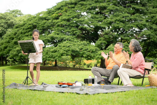 Happy Asian grandparents enjoying a picnic with their granddaughter in a green park