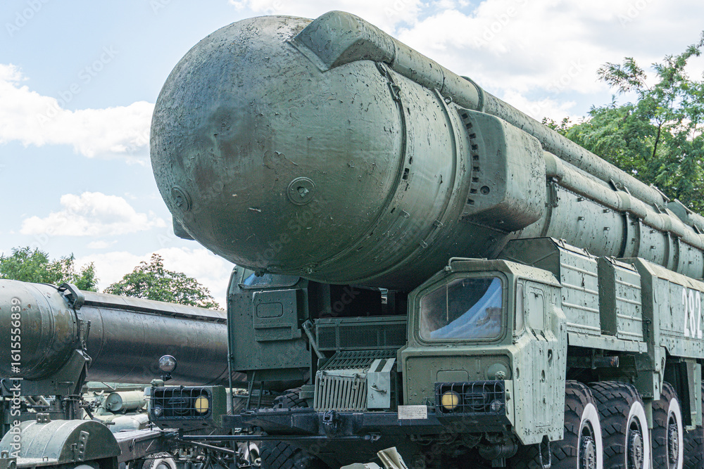 Naklejka premium Olive green military transport truck carrying a weathered ballistic missile on its platform in an outdoor setting with vegetation