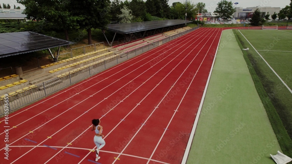 Fototapeta premium Jogging around the stadium, drone view. The woman is engaged in professional running