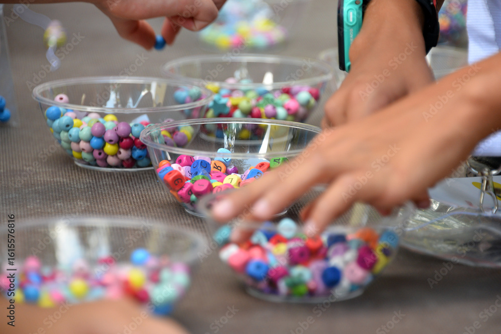 Obraz premium children's hands select multi-colored beads in bulk, bright balls of different shapes, craft material in transparent vases