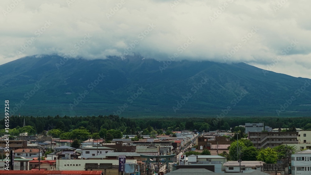 Obraz premium The city at the foot of Fujiyama. The top of the mountain is covered with clouds. Bird's-eye view of Japan's scenic nature
