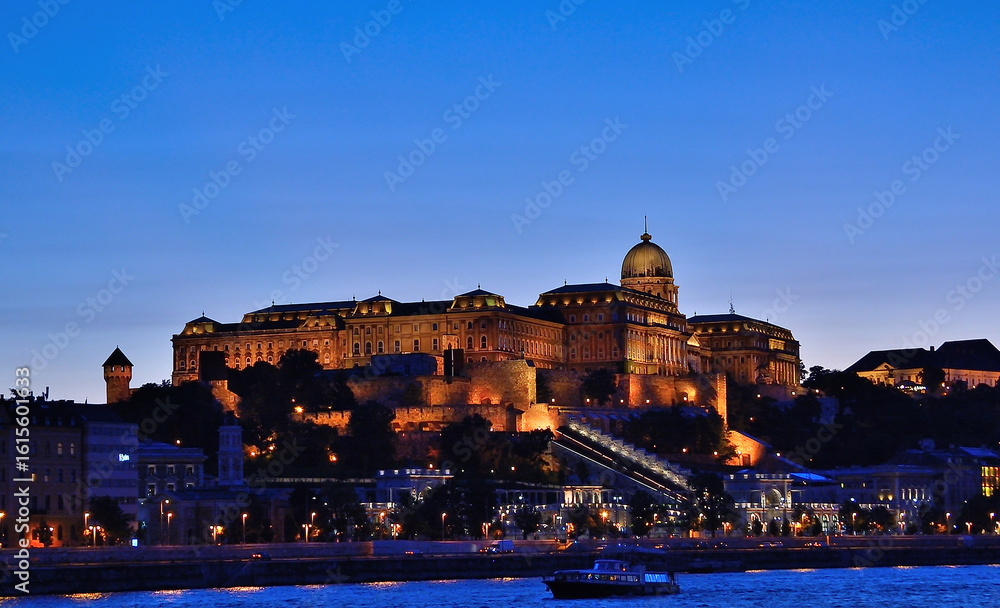 Fototapeta premium Buda castle illuminating the danube river at twilight in budapest